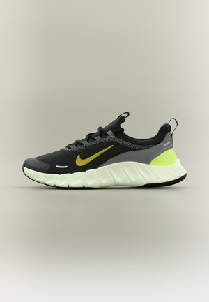 Chaussure de course Nike noire et grise avec un swoosh jaune, un détail de talon jaune néon et une semelle épaisse blanche amortissante sur un fond neutre.