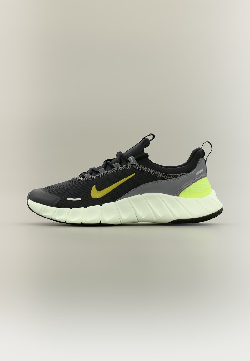 Μαύρο και γκρι παπούτσι για τρέξιμο Nike με κίτρινο σήμα, νεον κίτρινη λεπτομέρεια στη φτέρνα και παχύ άσπρο μαξιλαρωμένο πέλμα σε ουδέτερο φόντο.