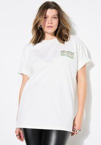 Camiseta de algodón blanca con mangas enrolladas y un gráfico en el pecho que dice "NO MIRES ATRÁS" en verde. Corte casual y holgado.