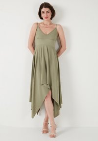 Olive green, knee-length dress with a v-neck, thin straps, and an asymmetrical hemline. Soft, textured fabric drapes elegantly.