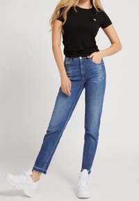 Sort bomuld t-shirt kombineret med falmede blå jeans med lige snit, slidte detaljer og frynset kant; båret med hvide sneakers.