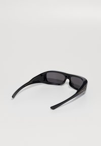 Crne sunčane naočale s plastičnim okvirom, tamnim lećama i aerodinamičnim dizajnom. Imaju reljefni "Oakley" logo sa strane.