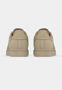 Beige Adidas sneakers featuring a smooth texture, tonal branding on the heel, and a low-profile design with a simple silhouette.