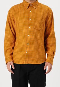 Camicia a righe in arancione e nero. Caratterizzata da un colletto, maniche lunghe e una tasca sul petto. Realizzata in un tessuto morbido e testurizzato.