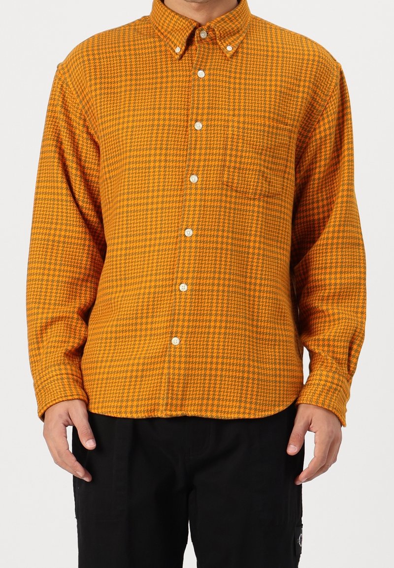Camicia a righe in arancione e nero. Caratterizzata da un colletto, maniche lunghe e una tasca sul petto. Realizzata in un tessuto morbido e testurizzato.