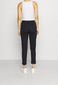 Dark gray elastic waist pants with a smooth texture, two back pockets, and a tapered leg design. Worn with white shoes and a tank top.