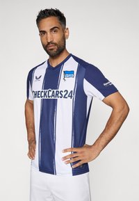 Sinine ja valge riba muster, spordisärk V-kaelusega, mille rinnal on "CHECKCARS24" logo ja "HerthaBSC" embleem. Tekstureeritud kangas.