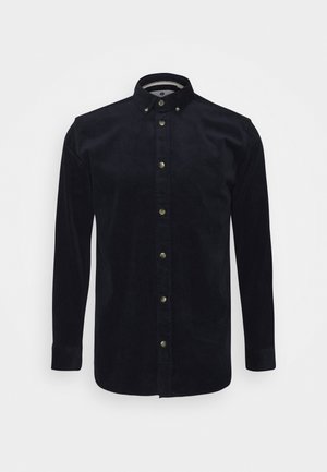 Camisa negra de pana de manga larga con cuello abotonado y botones metálicos en la parte delantera, mostrada sobre un fondo blanco.