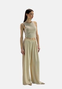 Beige cropped top met mouwloos ontwerp, gecombineerd met beige wijde broek met elastische tailleband en een subtiel textuurpatroon.