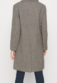 Abrigo de cuadros gris con corte recto, mangas largas y cuello con muesca. La tela tiene un patrón texturizado con tonos contrastantes.