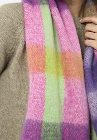 Gros plan sur une personne portant un pull beige et une écharpe douce et colorée avec des rayures roses, violettes, vertes et orange.