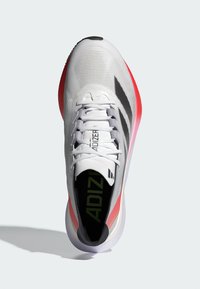 Zapatilla deportiva blanca con parte superior de malla, con cordones grises, un acento rojo y negro en la suela, y la marca "ADIZERO" en la lengüeta.