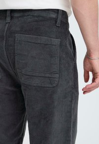 Gray corduroy pants featuring ribbed texture and a large back pocket. Cut with a straight fit, finished with belt loops and side seam pockets.