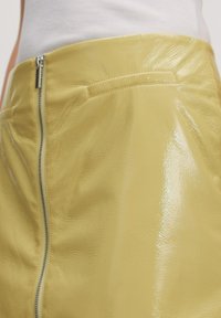 Geel faux leren rok met een glanzende, gestructureerde afwerking, voorzien van een zilveren ritssluiting aan de zijkant en een enkele voorzak.