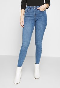 Calças de ganga de cintura alta, com uma silhueta ajustada, feitas de denim. Apresentam bolsos frontais e fecho éclair, combinadas com botas de tornozelo brancas.