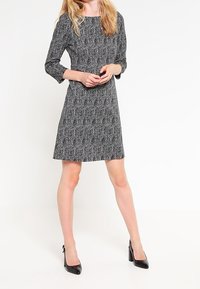 Musta-valkoinen herringbone-kuvioinen mekko, jossa on kolmivartiset hihat, A-linjainen siluetti, pehmeä kangas ja pyöreä kaula-aukko.
