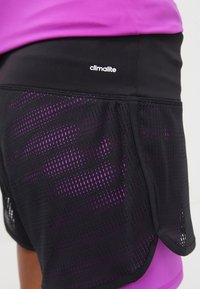 Schwarze Sportshorts mit Mesh-Textur, ausgestattet mit einer lila Unterschicht und weißem "climalite"-Logo. Glatter Bund, lockere Passform.