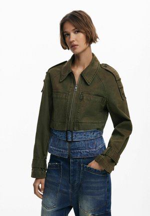 Olive green cropped jacket with a zip front and shoulder epaulettes, paired with blue denim high-waisted pants featuring front pockets.