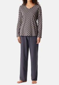Långärmad pyjamaströja i beige med ett mörkt geometriskt mönster; parat med löst sittande pyjamasbyxor i mörkgrått. Mjuk tygstruktur.