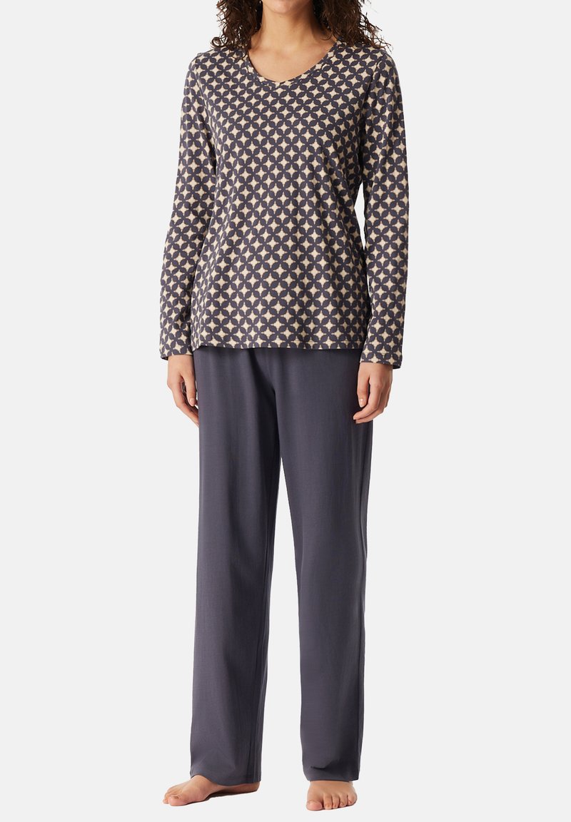 Långärmad pyjamaströja i beige med ett mörkt geometriskt mönster; parat med löst sittande pyjamasbyxor i mörkgrått. Mjuk tygstruktur.