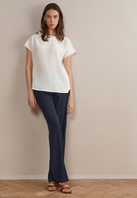 Biała bluzka na krótki rękaw w połączeniu z ciemnoniebieskimi spodniami o prostym kroju i brązowymi sandałami na paski. Gładkie tekstury i casualowy design.