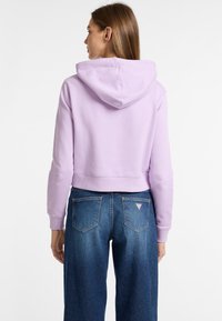 Sudadera lavanda corta con una gran capucha, puños y dobladillo acanalados, combinada con unos vaqueros de cintura alta en azul que presentan un logo triangular en el bolsillo.