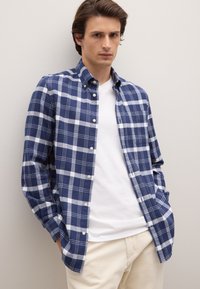 Kariertes Hemd in Marineblau und Weiß, im Button-Down-Stil, mit langen Ärmeln, aus gewebtem Stoff. Trägt man über einem weißen T-Shirt, kombiniert mit hellen Hosen.