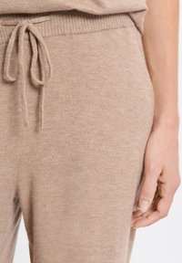 Beige gebreide joggingsbroek met een trekkoord in de taille, uitgerust met ribbelstructuur, zijzakken en een gladde stofafwerking langs het been.