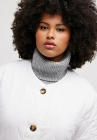 Prošívaná bílá bunda s šedým žebrovaným rolákem. Má kulaté hnědé knoflíky a texturovaný vzor na látce bundy.