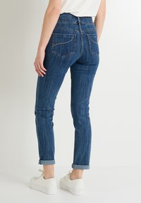 Jeans de tiro alto de color azul oscuro con un corte ajustado, que presentan dos bolsillos traseros y puños doblados, combinados con zapatillas blancas.