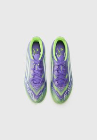 Des chaussures de football violettes avec une surface texturée, présentant des accents verts et un motif géométrique. Les lacets sont violets ; le logo est visible.
