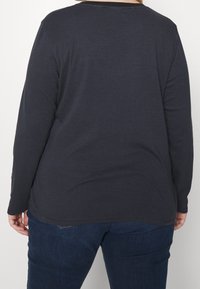 Pitkähihaisesta tummansinisestä paidasta, jossa on ohuita vaakaraitoja. Paidassa on pyöreä pääntie ja rento malli, ja se on valmistettu pehmeästä kankaasta.