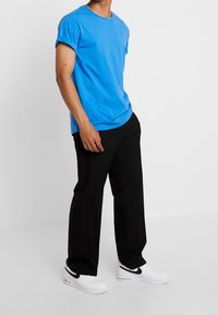 Blå bomullströja med uppvikta korta ärmar, i kombination med svarta byxor och vita sneakers. Enkel design utan mönster eller accenter.