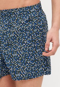 Shorts fleuris avec un fond noir, ornés de petites fleurs bleues et blanches, taille élastique et coupe décontractée.