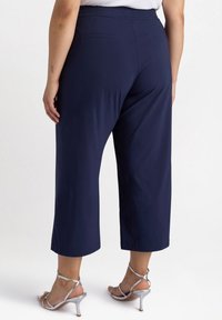 Mörkblå, cropped byxor med elastisk midja, med två bakfickor och en mjuk textur, tillsammans med silverfärgade remsandaler.