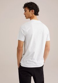Camiseta de manga corta gris claro con una textura suave; cuello redondo. Combinada con pantalones negros, vista desde la parte trasera.