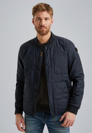 Chaqueta acolchada de color azul marino con estilo bomber, que cuenta con cierre de cremallera, cuello de canalé y bolsillos laterales; elaborada en tejido de nailon.