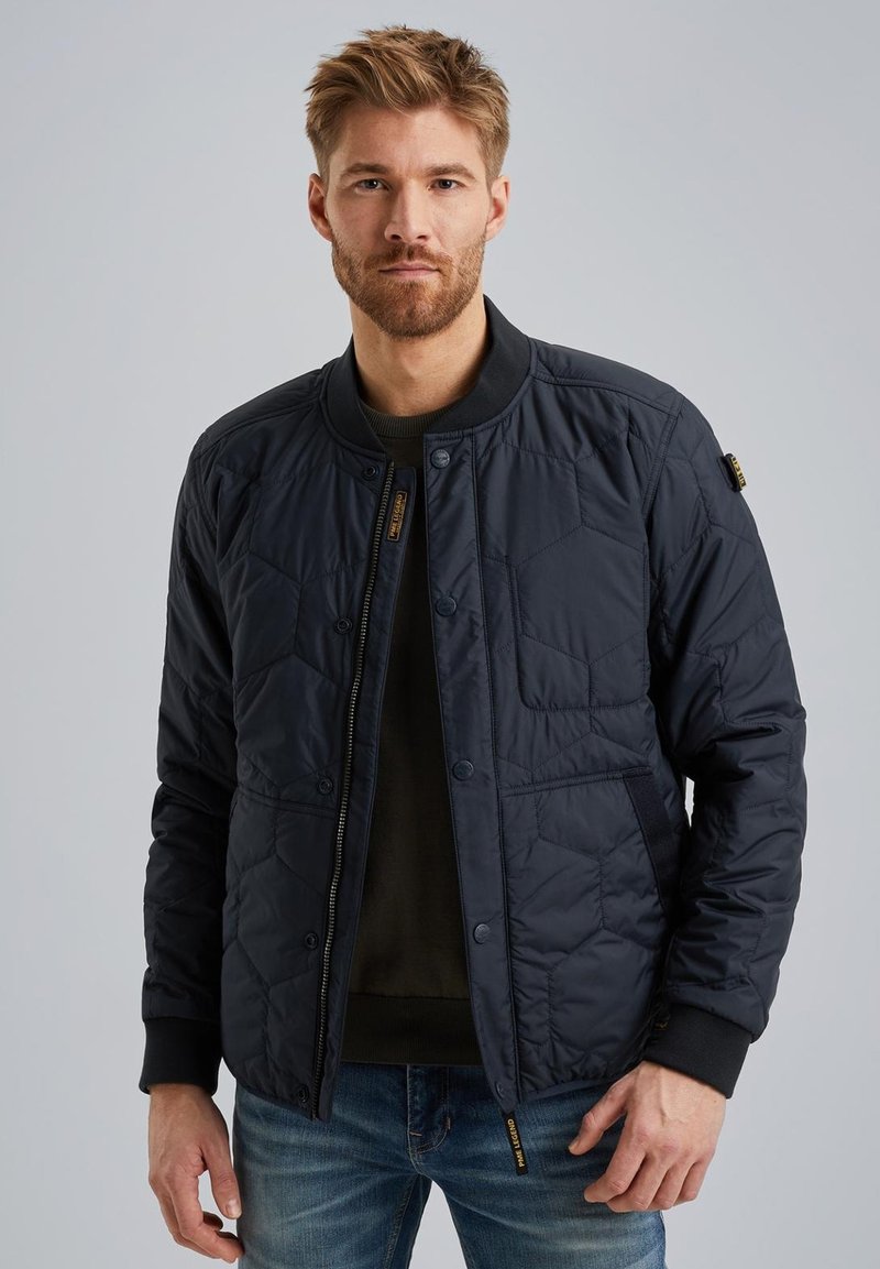 Marineblau gesteppte Bomberjacke mit Reißverschluss vorne, geripptem Kragen und Seitentaschen; aus Nylon gefertigt.