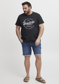 Svart bomullströja med vita textgrafik, kombinerad med upprullade denimshorts. Skorna består av bruna sandaler med remmar.