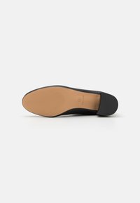 Zapato plano negro con parte superior lisa, puntera redondeada y suela de goma plana. La parte inferior presenta surcos horizontales para mejorar la tracción.