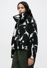 Μαύρο και άσπρο μοτίβο σε φλις μπουφάν με ψηλό γιακά, κλείσιμο με φερμουάρ και κοντό σχέδιο, με απαλό, υφή επιφάνειας.