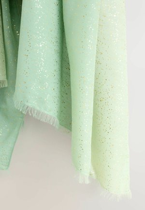 Světlé zelené plátno s metalickým zlatým vzorem posetým tečkami, s třásnitým okrajem a hladkou texturou. Zmačkané záhyby zvýrazňují design.