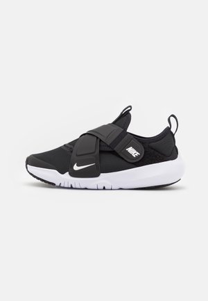 Chaussure de sport Nike noire et blanche avec large bride ajustable et fermeture velcro, semelle coussinée et languettes sur la languette et le talon.