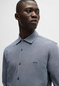 Camisa polo azul de manga corta, con tejido texturizado, con cuello y tres botones, logotipo grabado "BOSS" en el lado izquierdo del pecho.