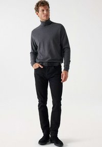 Sivi pulover s visokim ovratnikom uparen s crnim trapericama i crnim čizmama. Pulover ima duge rukave i uski kroj, stvarajući glatku siluetu.