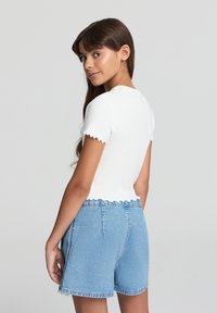 Top corto bianco a costine con bordi scallop abbinato a pantaloni shorts in denim blu chiaro. Gli shorts presentano un design a vita alta e orlo grezzo.