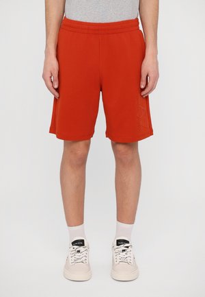 Shorts rouges en tissu doux, dotés d'une taille élastique et d'un léger logo en relief sur le côté. Longueur mi-cuisse.