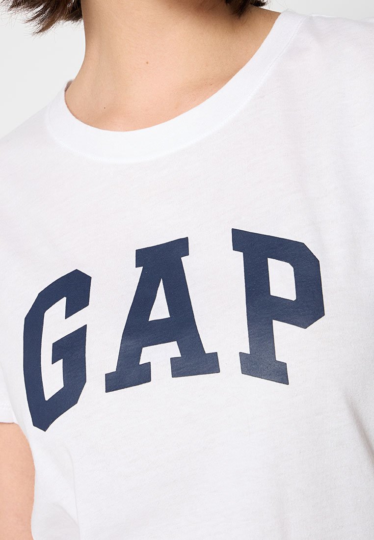 Camiseta blanca de algodón con letras navy en negrita que dicen "GAP" en el pecho. Mangas cortas y escote redondo.