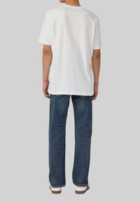Witte katoenen t-shirt met een ronde hals, gecombineerd met een blauwe denim jeans. De jeans hebben een rechte pijpdesign en een subtiele textuur.