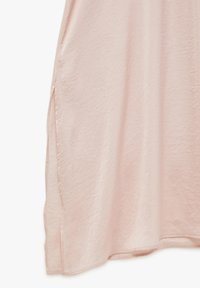 Hellrosa Kleid aus weichem, strukturiertem Stoff. Verfügt über Seitenschlitze und ein fließendes Design, mit einem Saum, der sanft gewölbt ist.